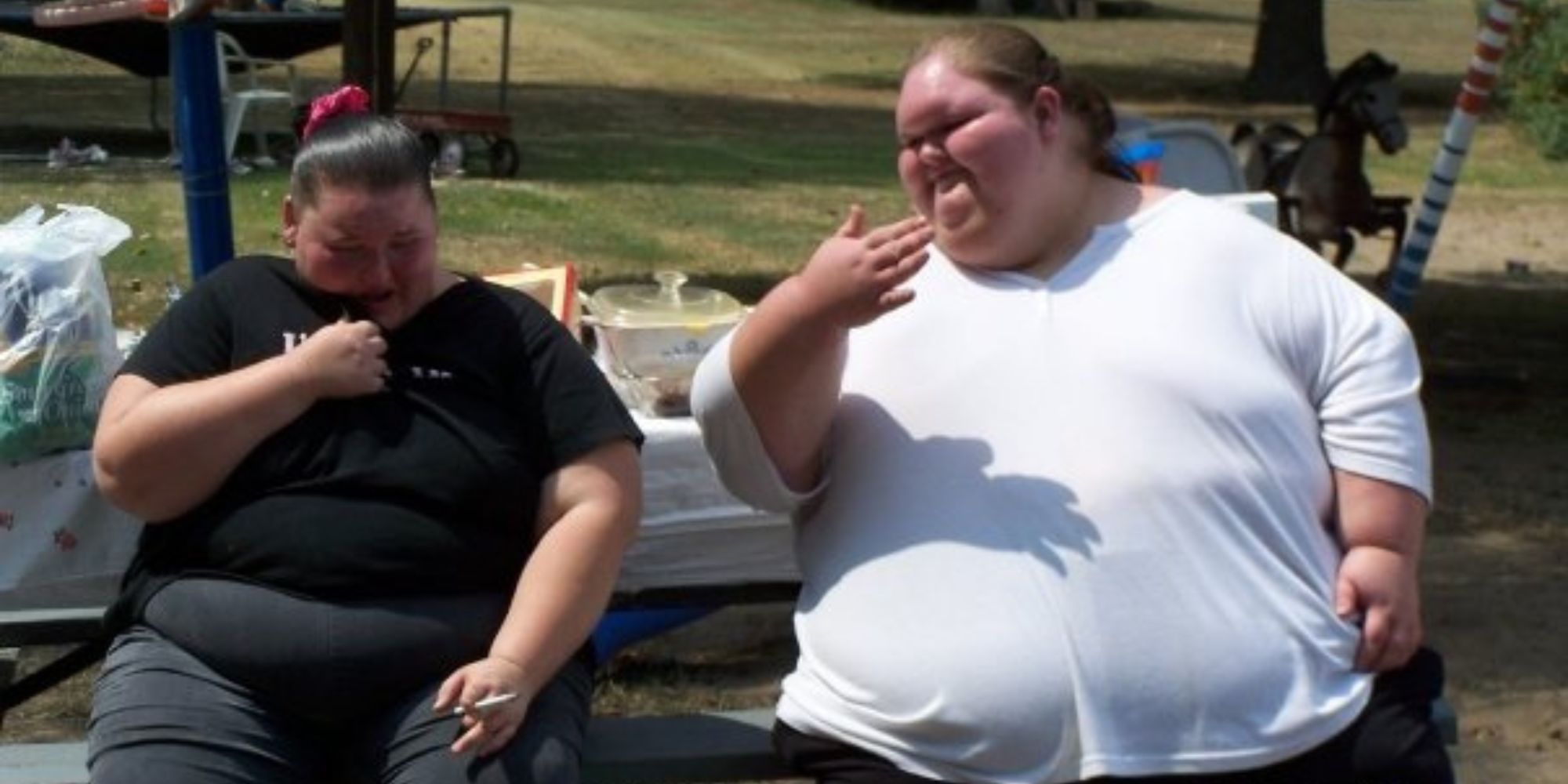1000-lb Sisters Amy Slaton & Tammy Slaton sitting on a bench side by side, Amy is smoking a cigarette