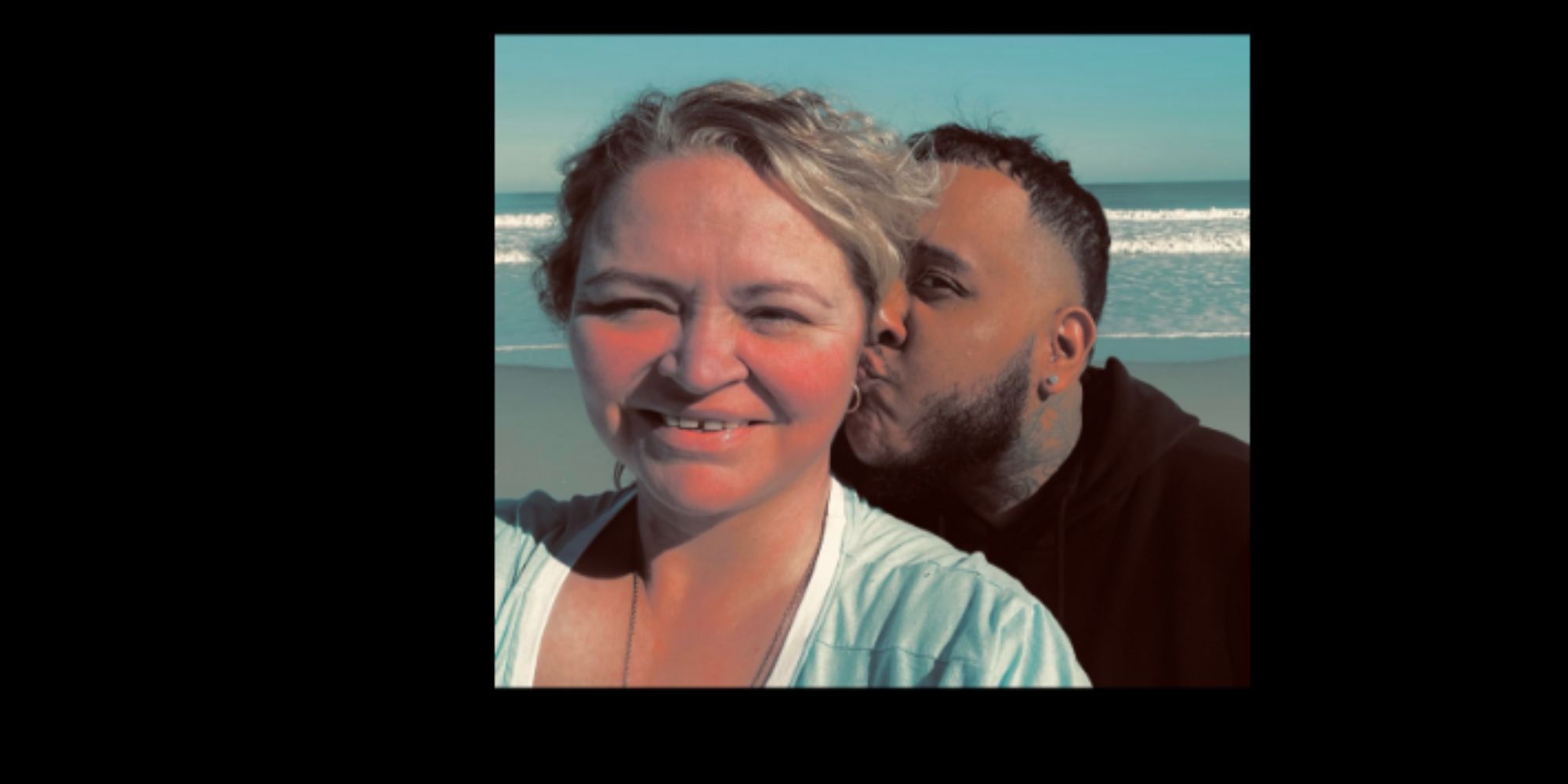 Irmãs Amanda Halterma de 1.000 libras na praia com RJ, ele beija a nuca dela, os dois olham para a câmera