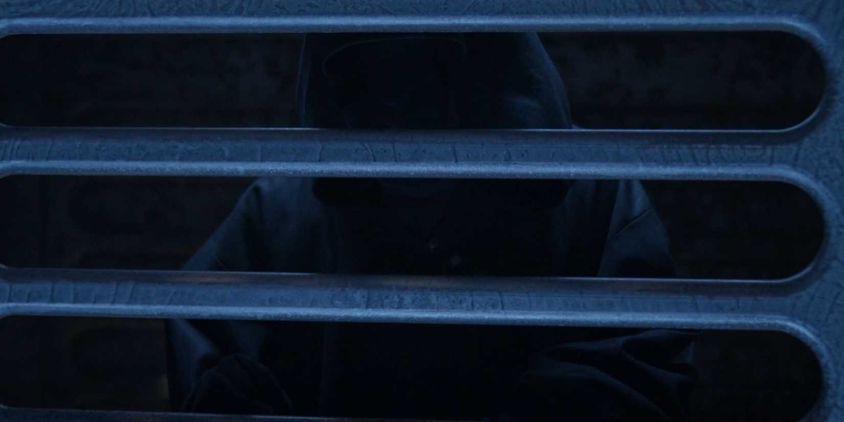 The Mantid in Resident Alien with his hood up behind bars