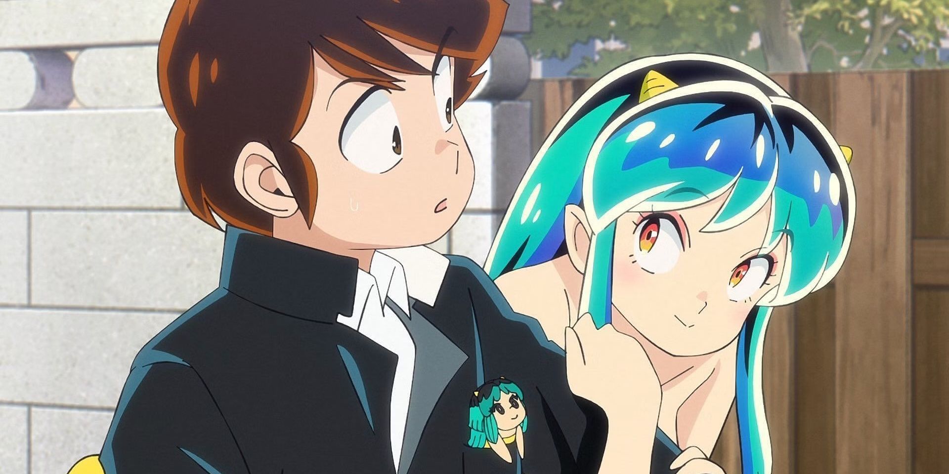 Lum wraps her arms around Ataru's left arm, with the latter dressed in a school uniform, as they stand outdoors in a neighbourhood