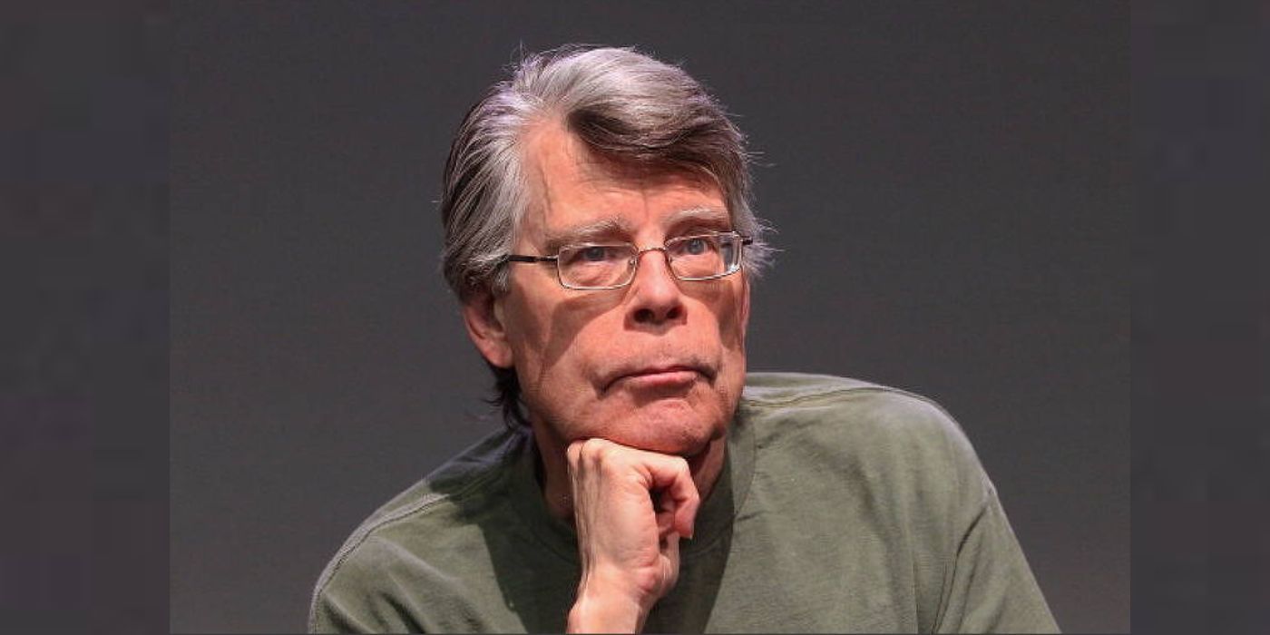Stephen King sitting against a gray backdrop with his chin propped on his fist