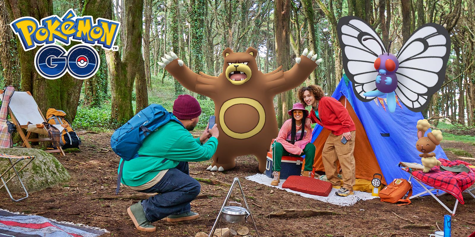 Duas pessoas posando ao lado de uma barraca com o Pokémon Ursaring em pé sobre seus ombros, outra pessoa está ajoelhada tirando uma foto em seu telefone.