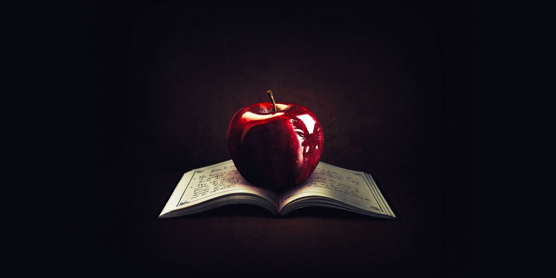 Uma maçã brilhante refletindo o contorno de um shinigami sentado em cima de um livro. 