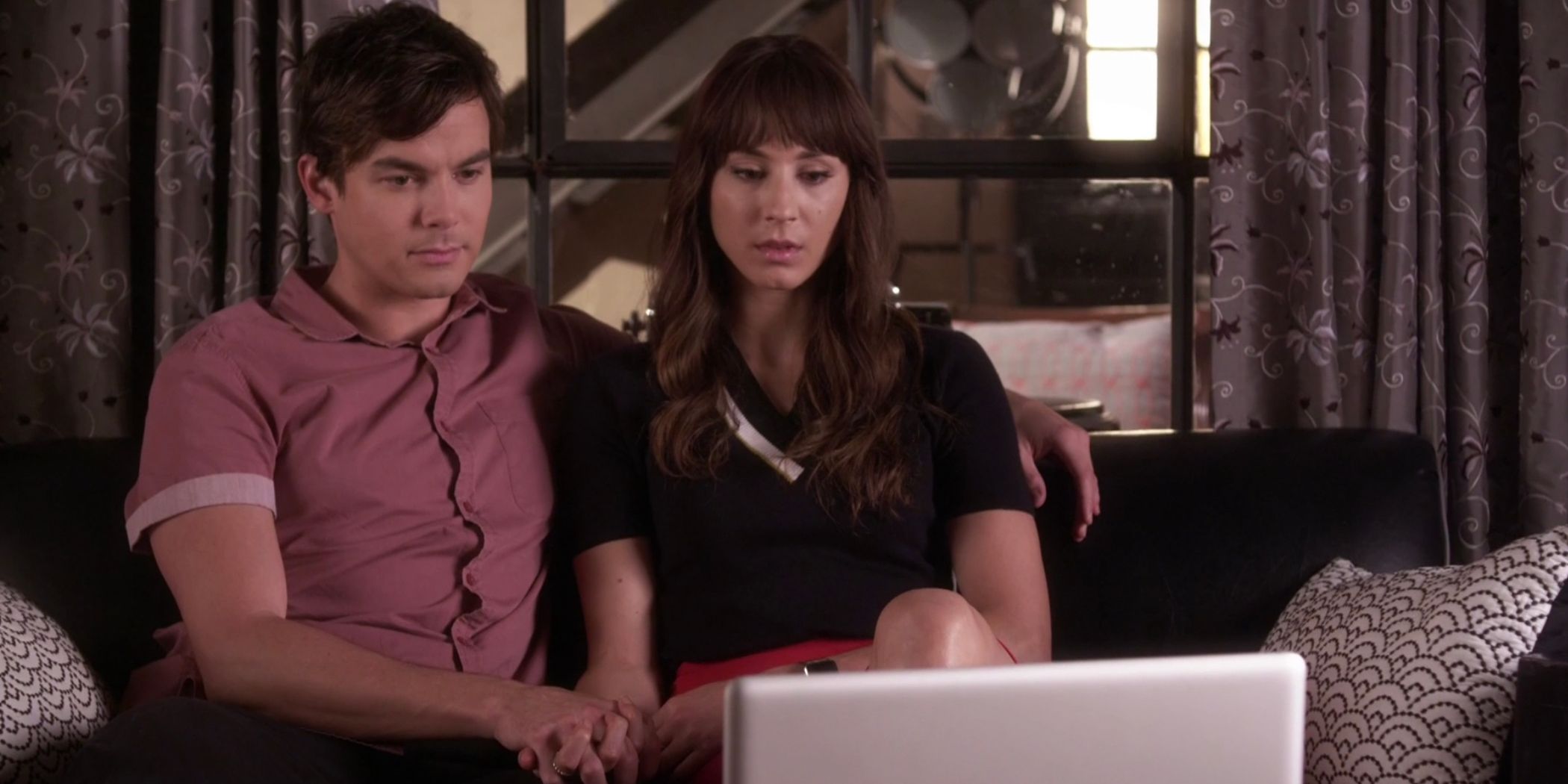 Caleb e Spencer sentados de frente para um laptop e de mãos dadas em Pretty Little Liars