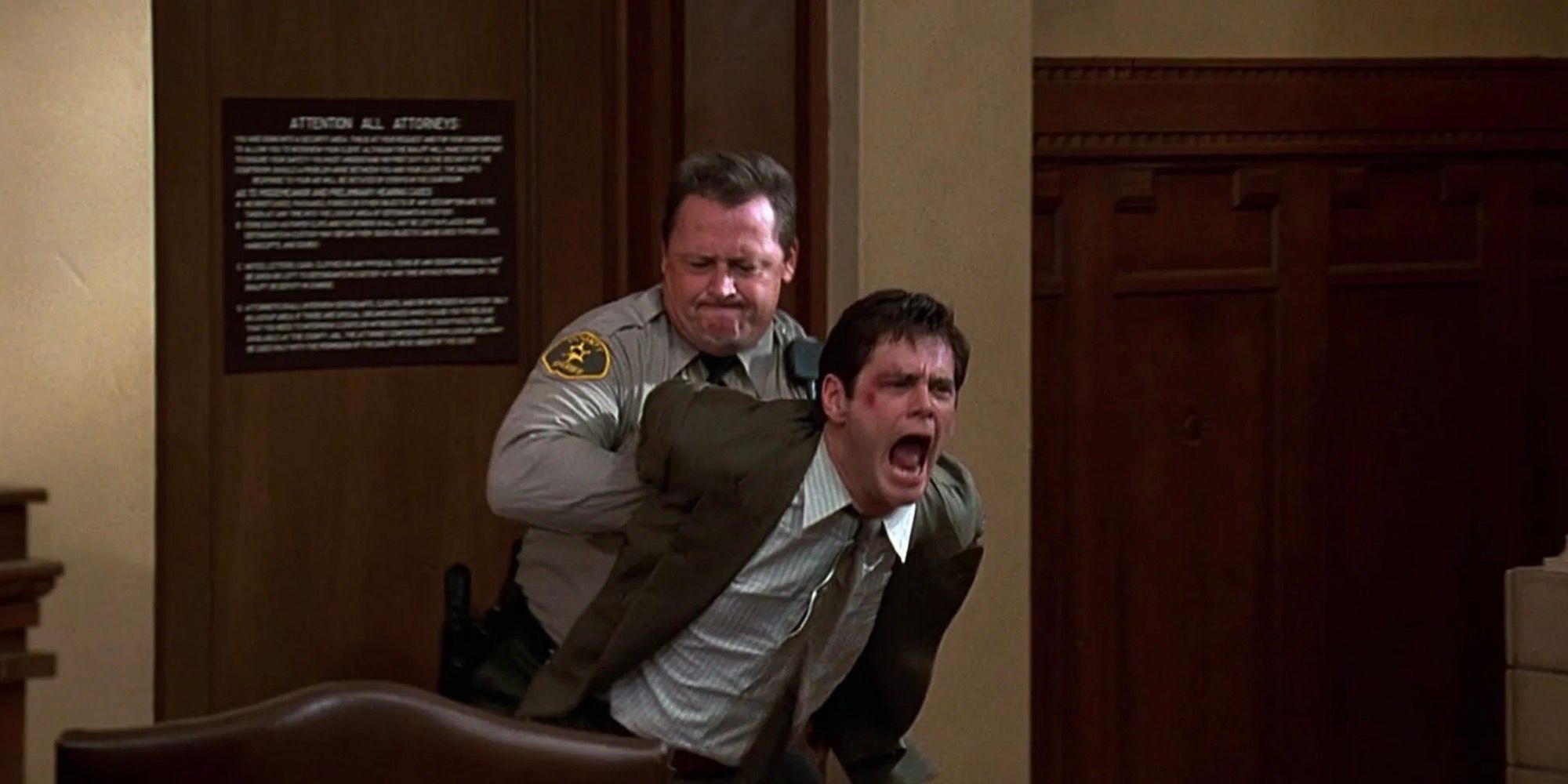 Jim Carrey é arrastado para fora do tribunal por um oficial de justiça. 
