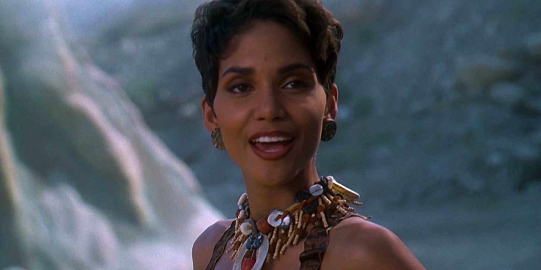 Flintstones Halle Berry wearing a beaded necklace and circular earrings and smiling towards the camera