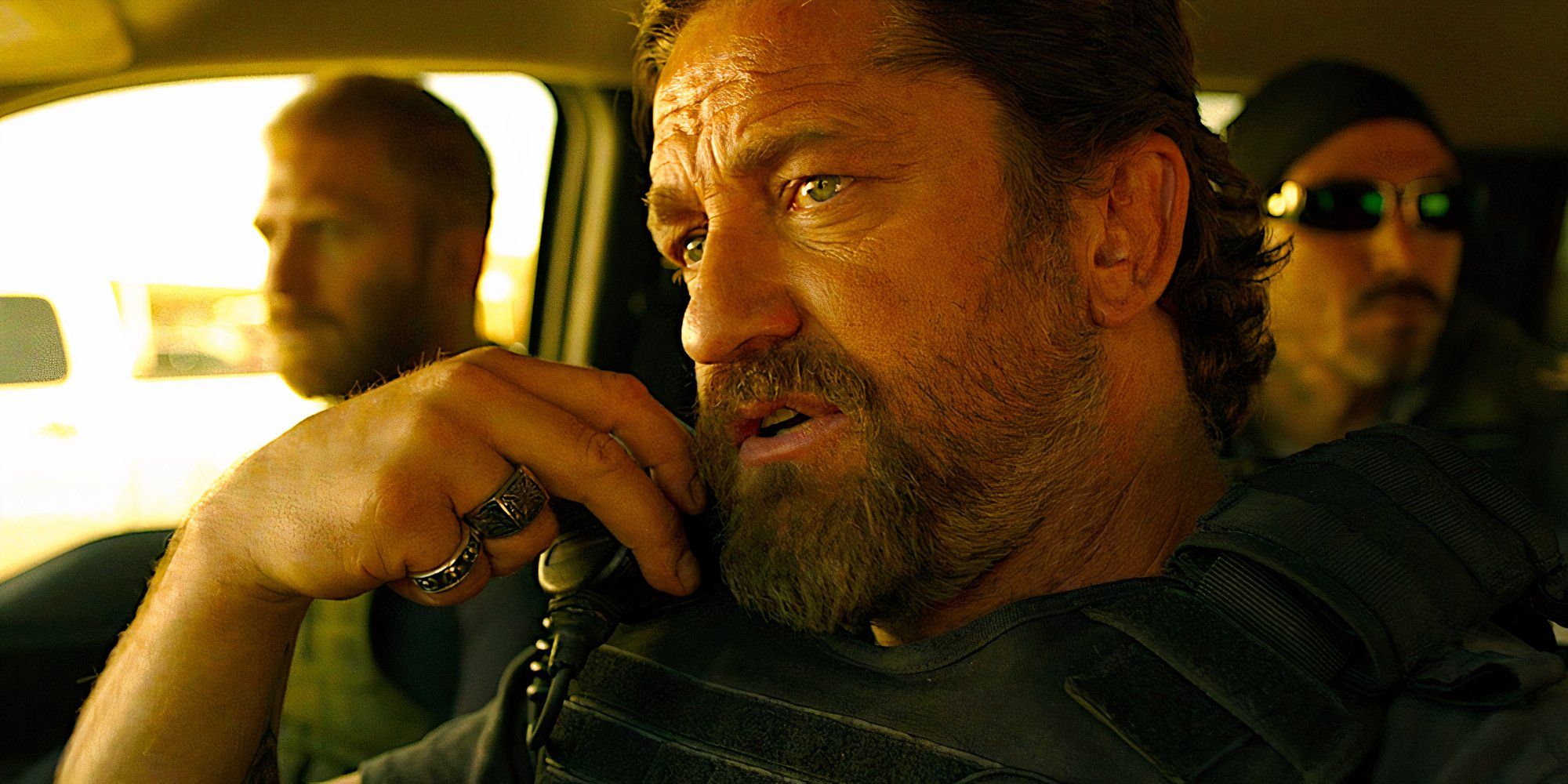 Gerard Butler talks on a radio while riding in a car in a scene from Den of Thieves