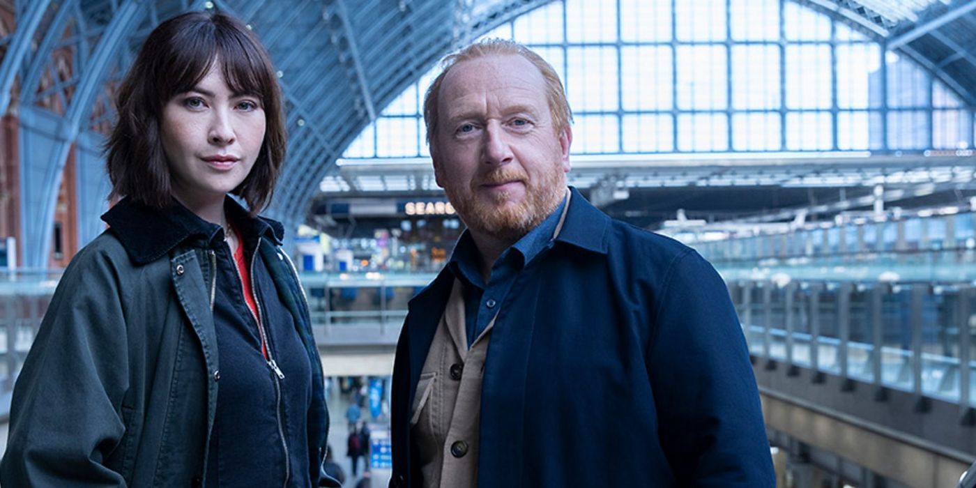 Layla (Vanessa Emme) and Max (Adrian Scarborough) standing together in a train station in The Chelsea Detective.