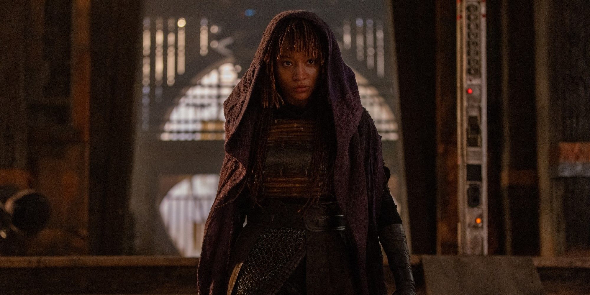 Mae (Amandla Stenberg) stands in front of an entryway while wearing her hood in The Acolyte
