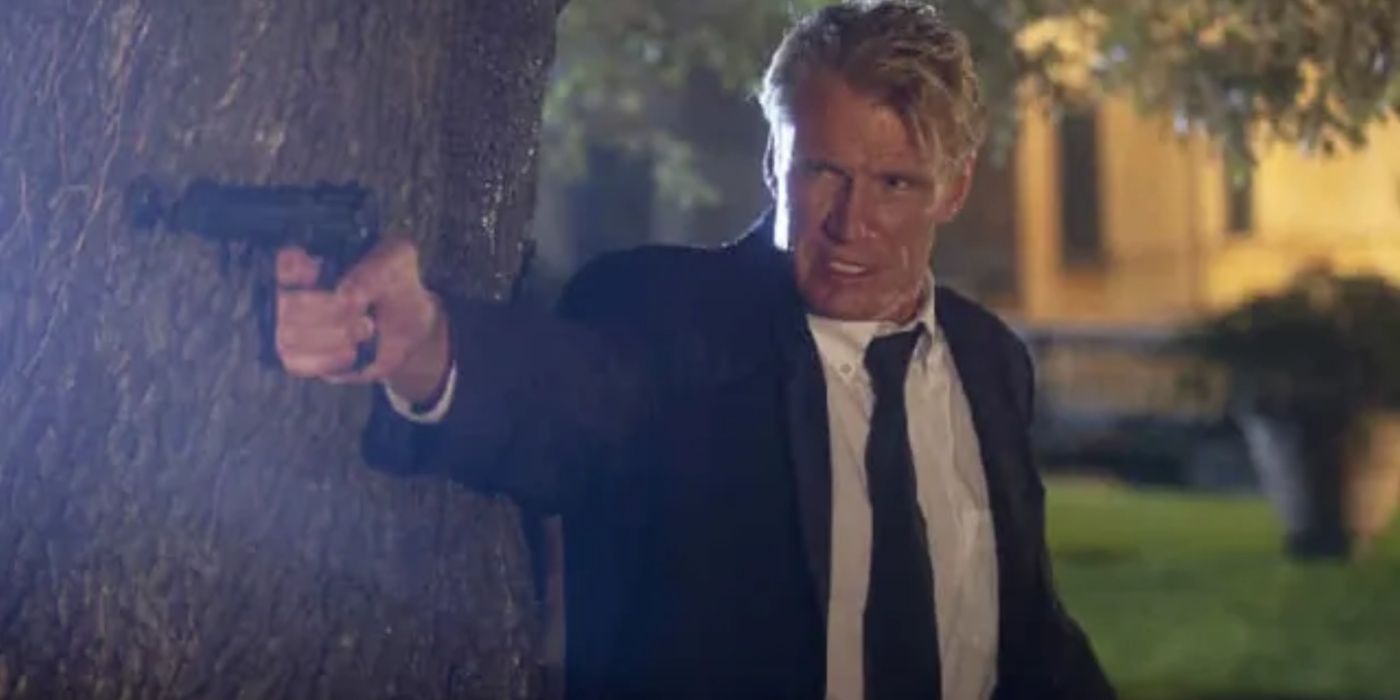 Johansen (Dolph Lundgren) taking cover behind a tree and pointing a gun in Wanted Man