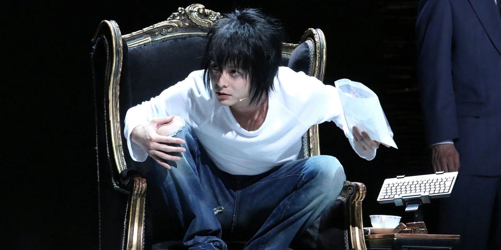 Live action L sentado em uma cadeira do Death Note o musical. 