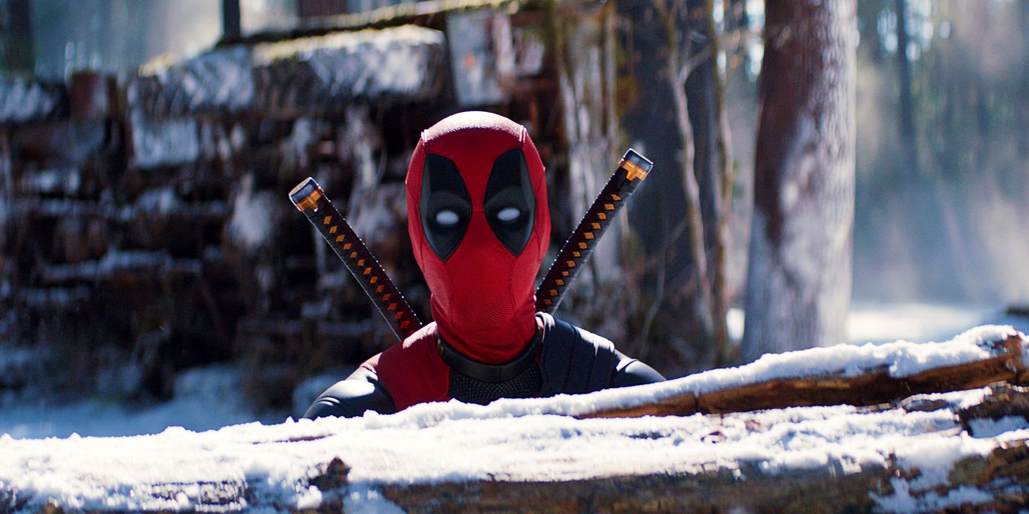 Ryan Reynolds In Deadpool Costume Poking His Head Up From Behind A Snowy Log In Deadpool & Wolverine
