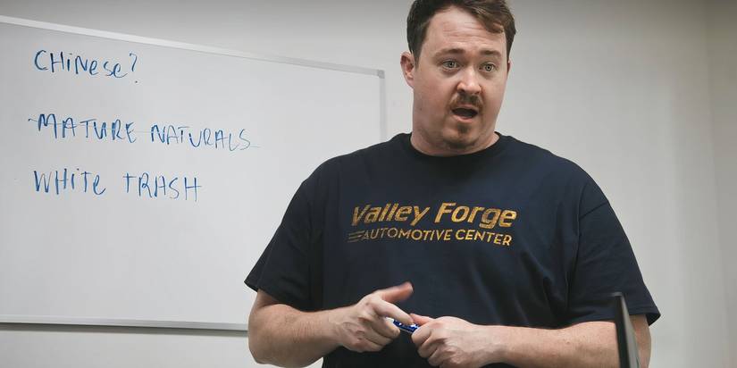 Shane stands at a whiteboard on the wall with a marker in his hand. The white board says “CHINESE?” “MATURE NATURALS” and “WHITE TRASH”