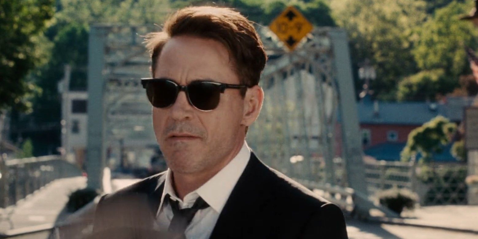 Hank (Robert Downey Jr.) bites his lip while wearing a suit and sunglasses in front of a bridge in The Judge (2014)