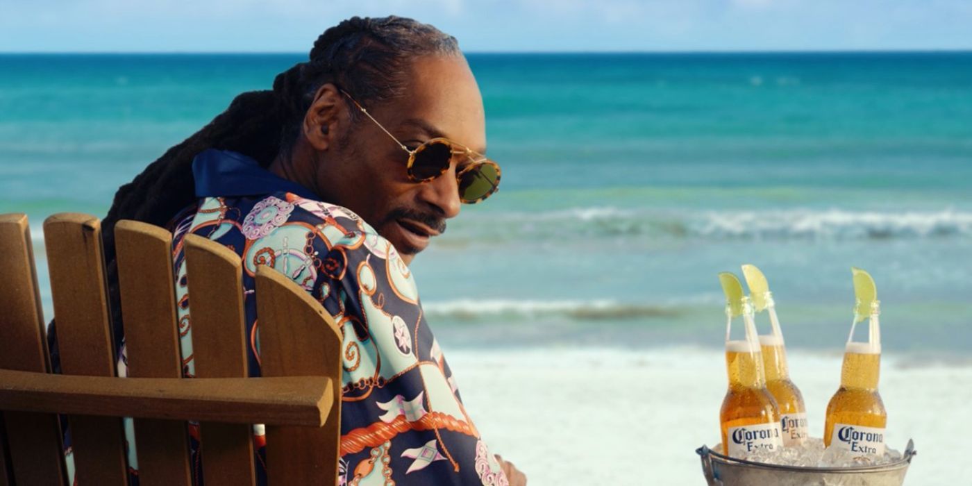 Snoop Dogg sitting on the beach and looking over his shoulder with a bucket of Coronas next to him in a Corona commercial.