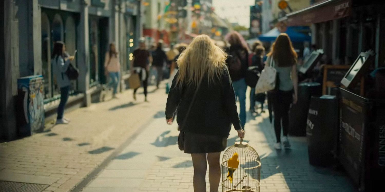 Nina holding her birdcage, walking down the street in The Watchers