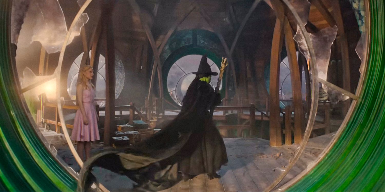 Elphaba (Cynthia Erivo) in her witch costume holding her magic broom, seen through a circular window with broken glass in Wicked 