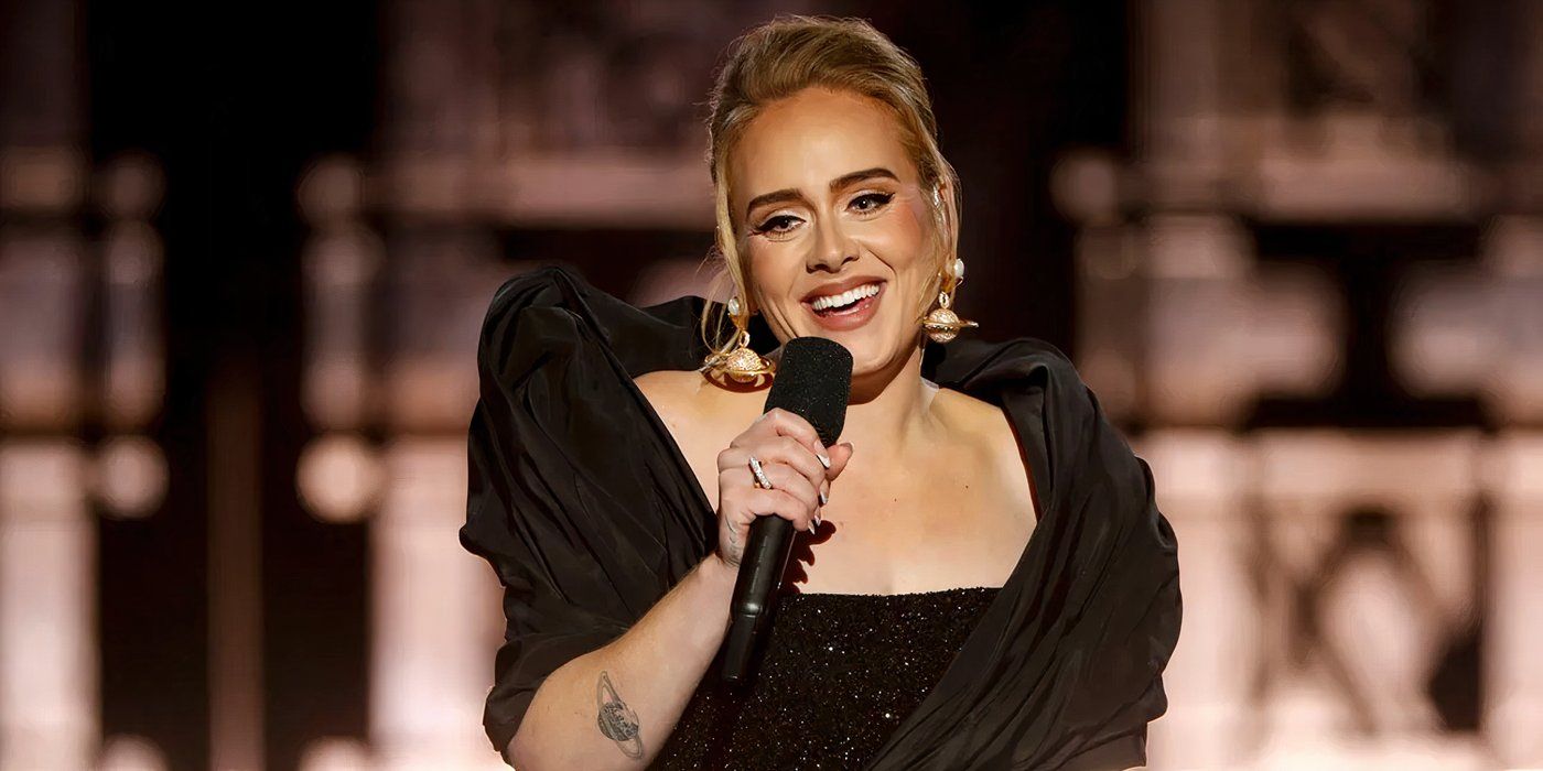 Adele canta en el escenario sosteniendo un micrófono y sonriendo