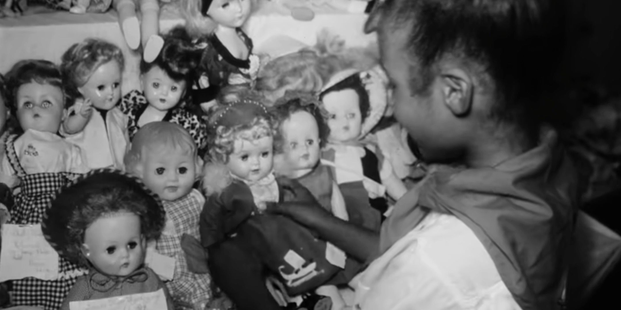 An old video shows a young girl picking up a baby doll. 