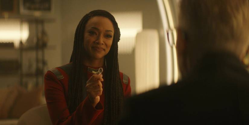 Captain Michael Burnham (Sonequa Martin-Green) holds up the infinity pager in Dr. Kovich's (David Cronenberg) office Star Trek Discovery