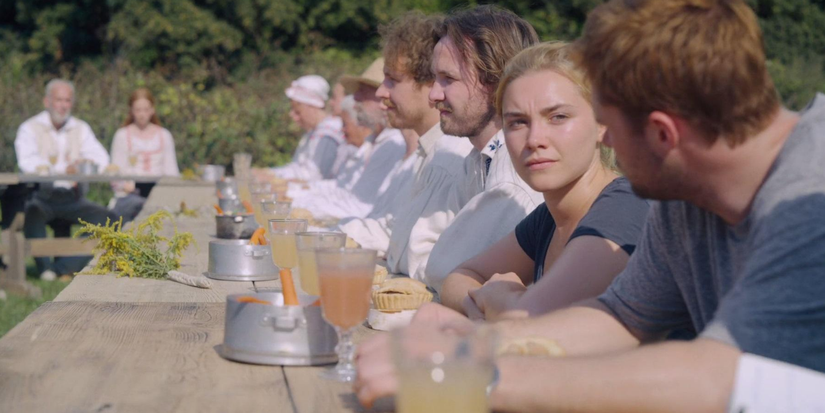 Florence Pugh as Dani sits at a table with Christian and the Harga cult in Midsommar