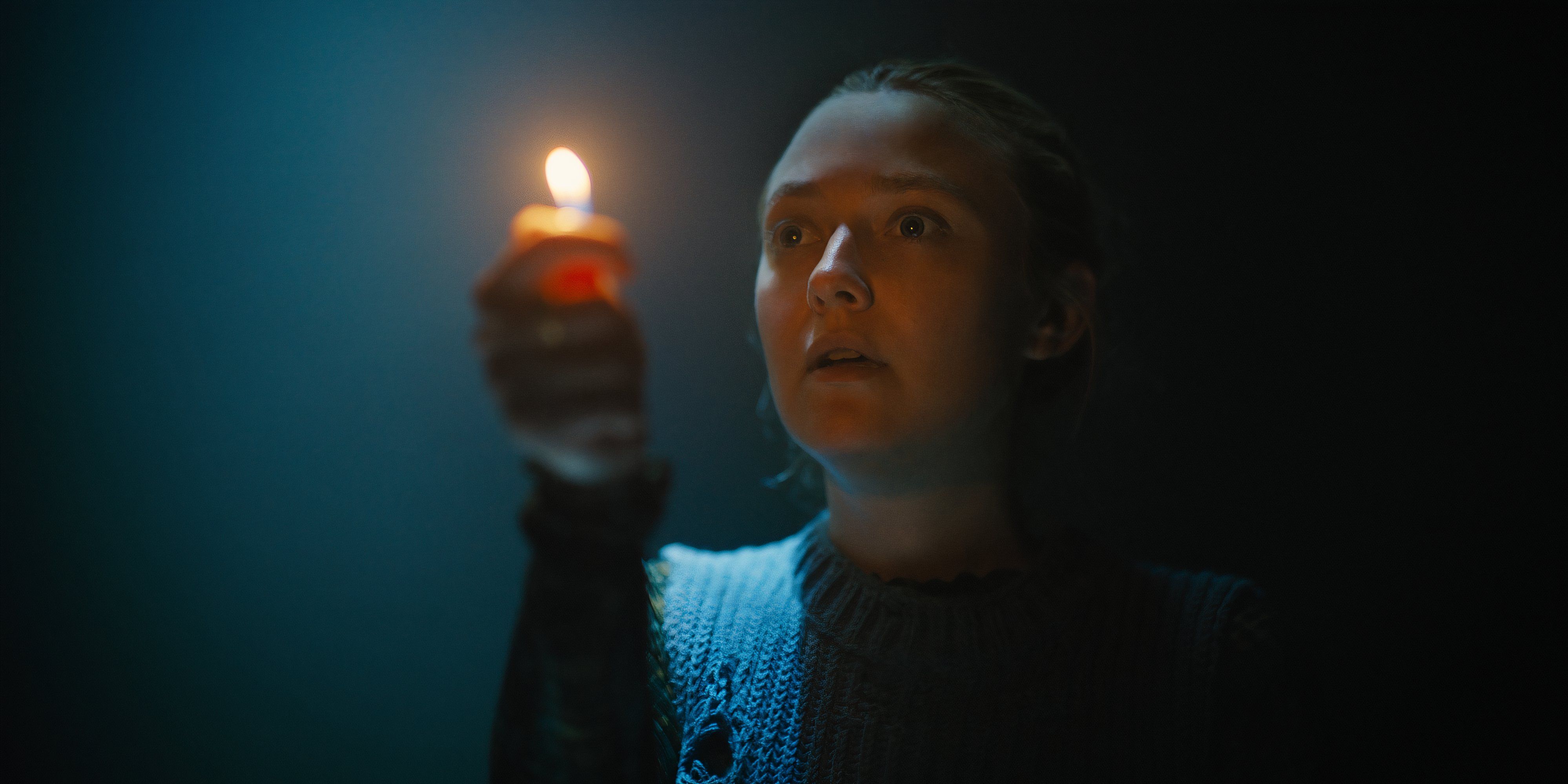 Dakota Fanning holds a candle up in The Watchers movie still