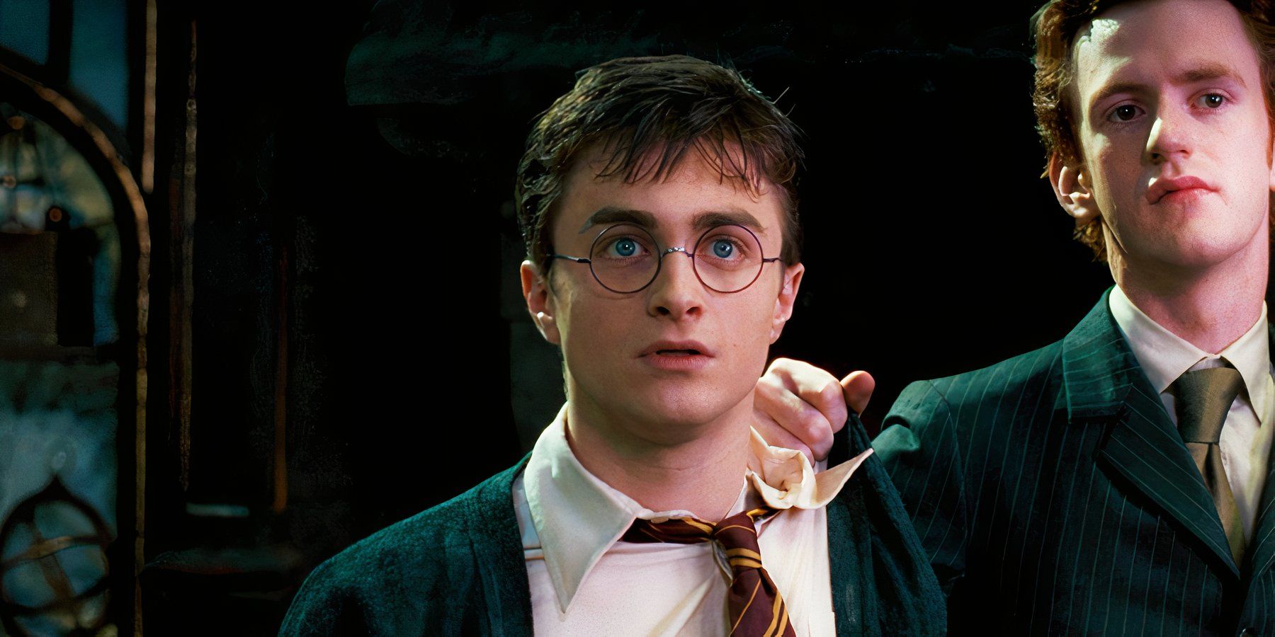 Daniel Radcliffe como Harry Potter parecendo nervoso com Percy (Chris Rankin) colocando a mão em seu ombro em Harry Potter e a Ordem da Fênix