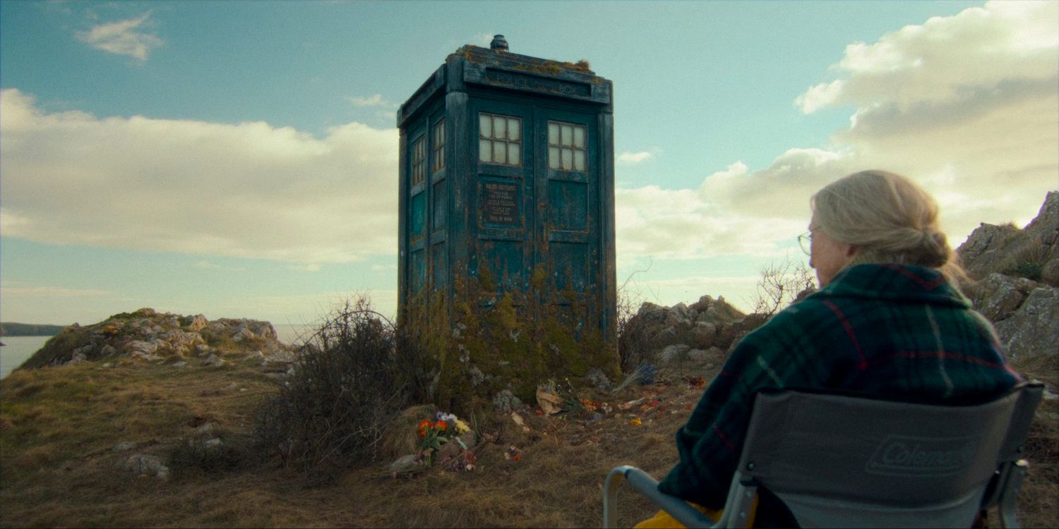 Ruby idosa sentada em frente à TARDIS abandonada na costa do País de Gales no episódio 4 da 14ª temporada de Doctor Who