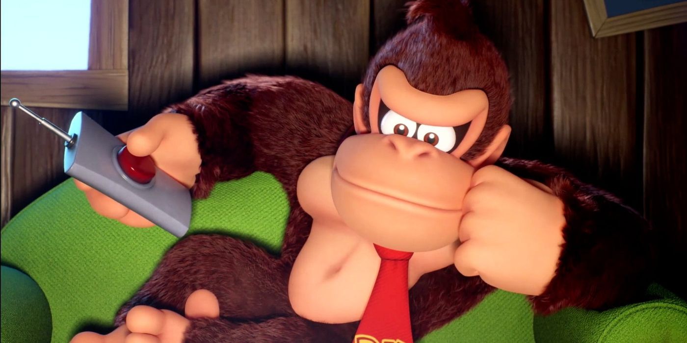 Donkey Kong está sentado en el sofá, sosteniendo un control remoto con un gran botón rojo.