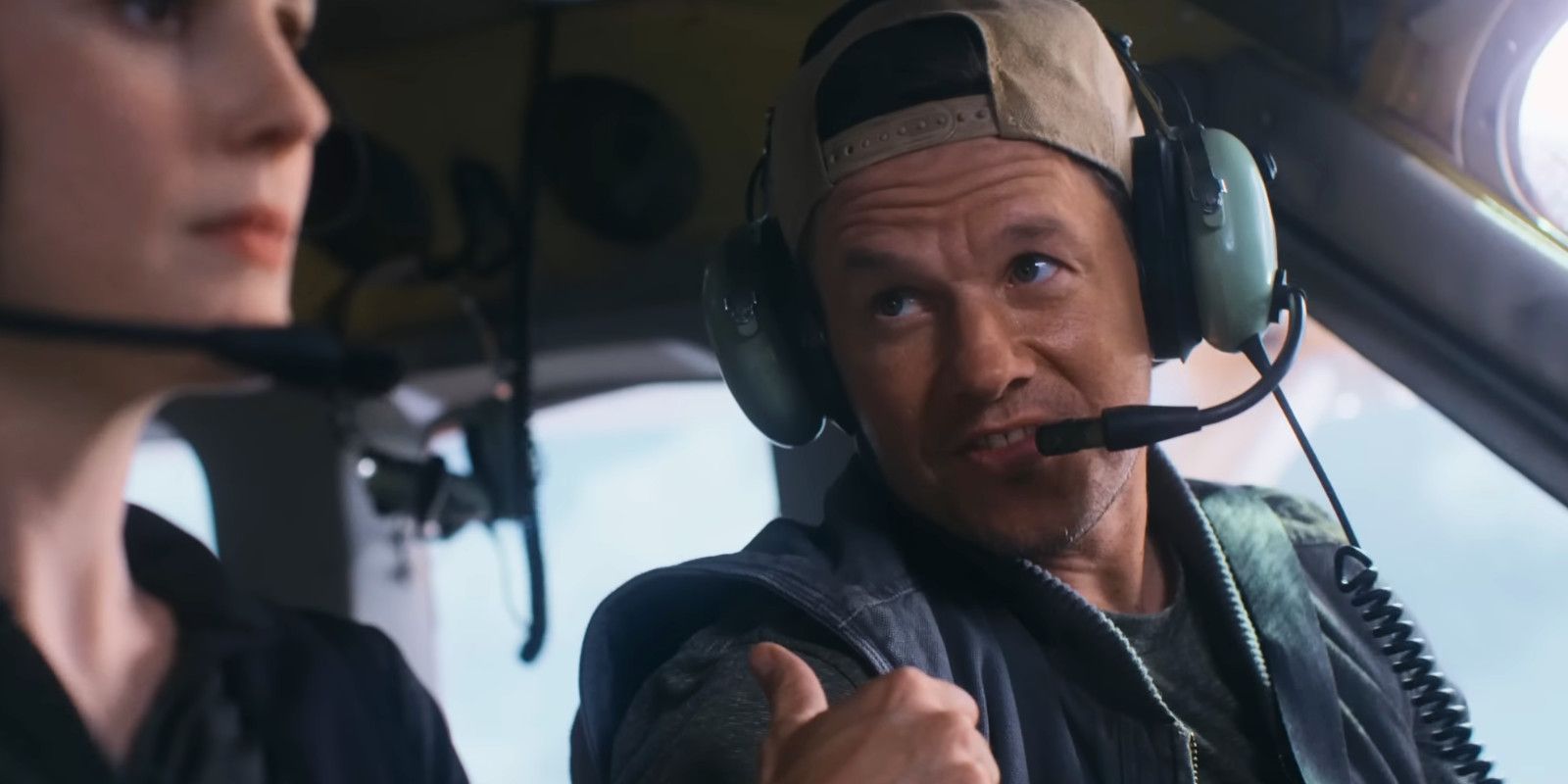 Mark Wahlberg mengacungkan jempol dan mengenakan topi pilot di kokpit pesawat dalam Flight Risk