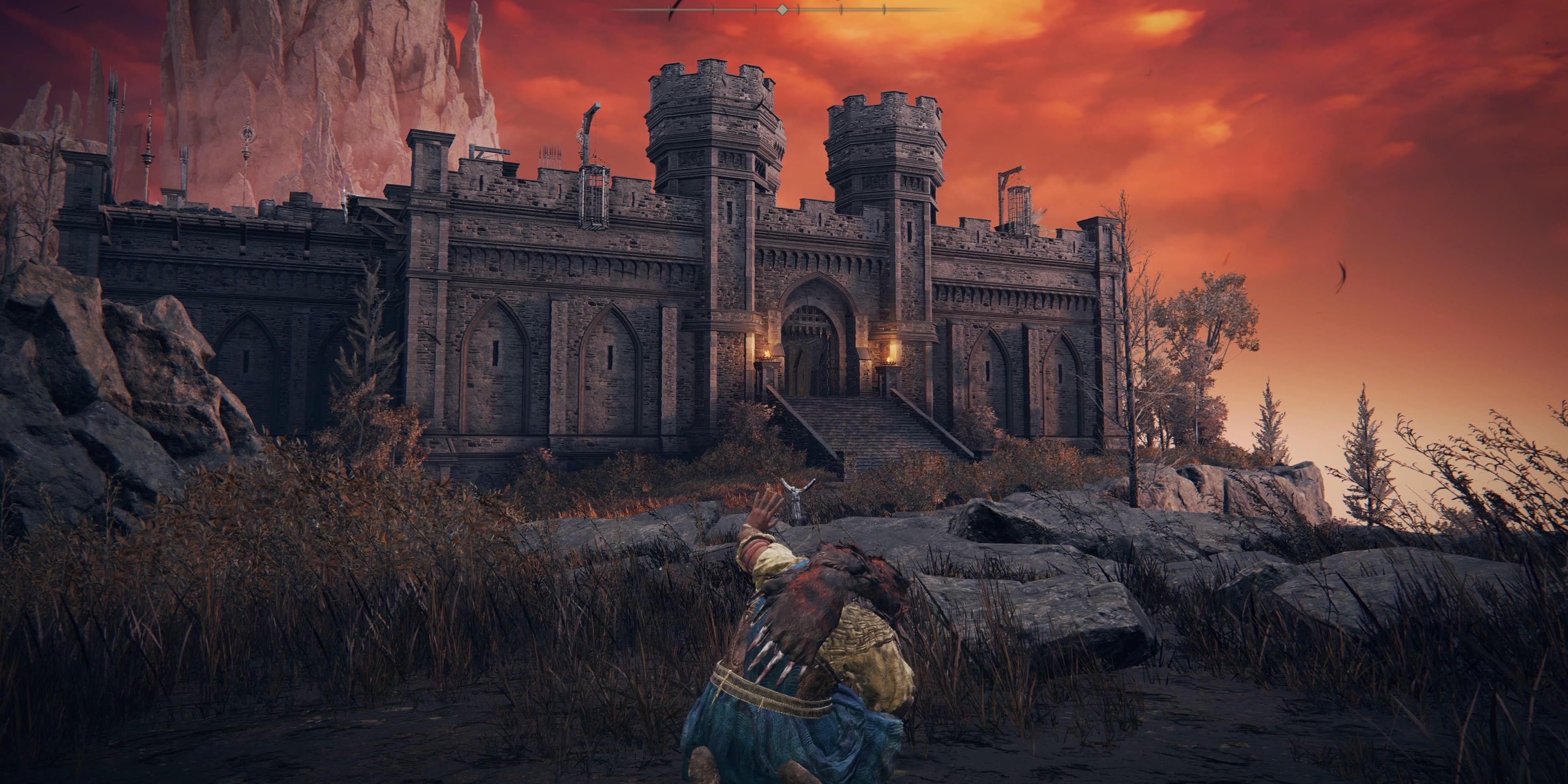 Karakter pemain dalam Elden Ring meringkuk di depan benteng batu gelap yang jongkok. Langit berwarna merah muda dan Jagged Peak dapat terlihat di latar belakang.