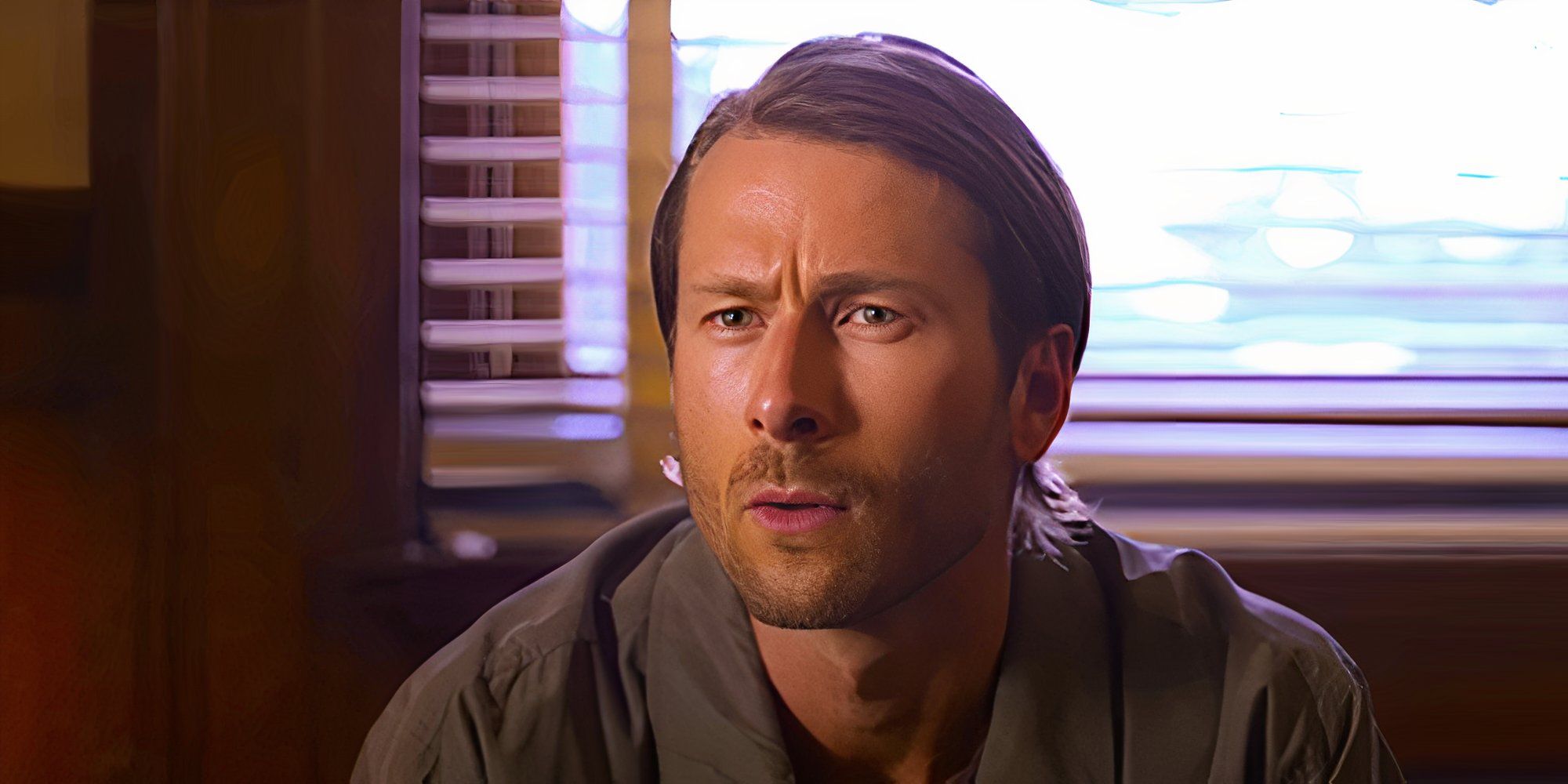 Glen Powell wears a puzzled expression while conversing in a scene from Hit Man