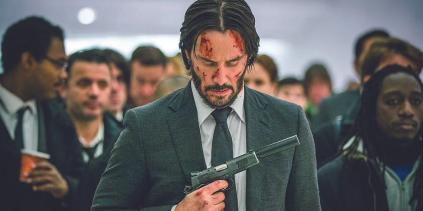 um John Wick ensanguentado segura uma arma e olha para ela em John Wick: Capítulo 2