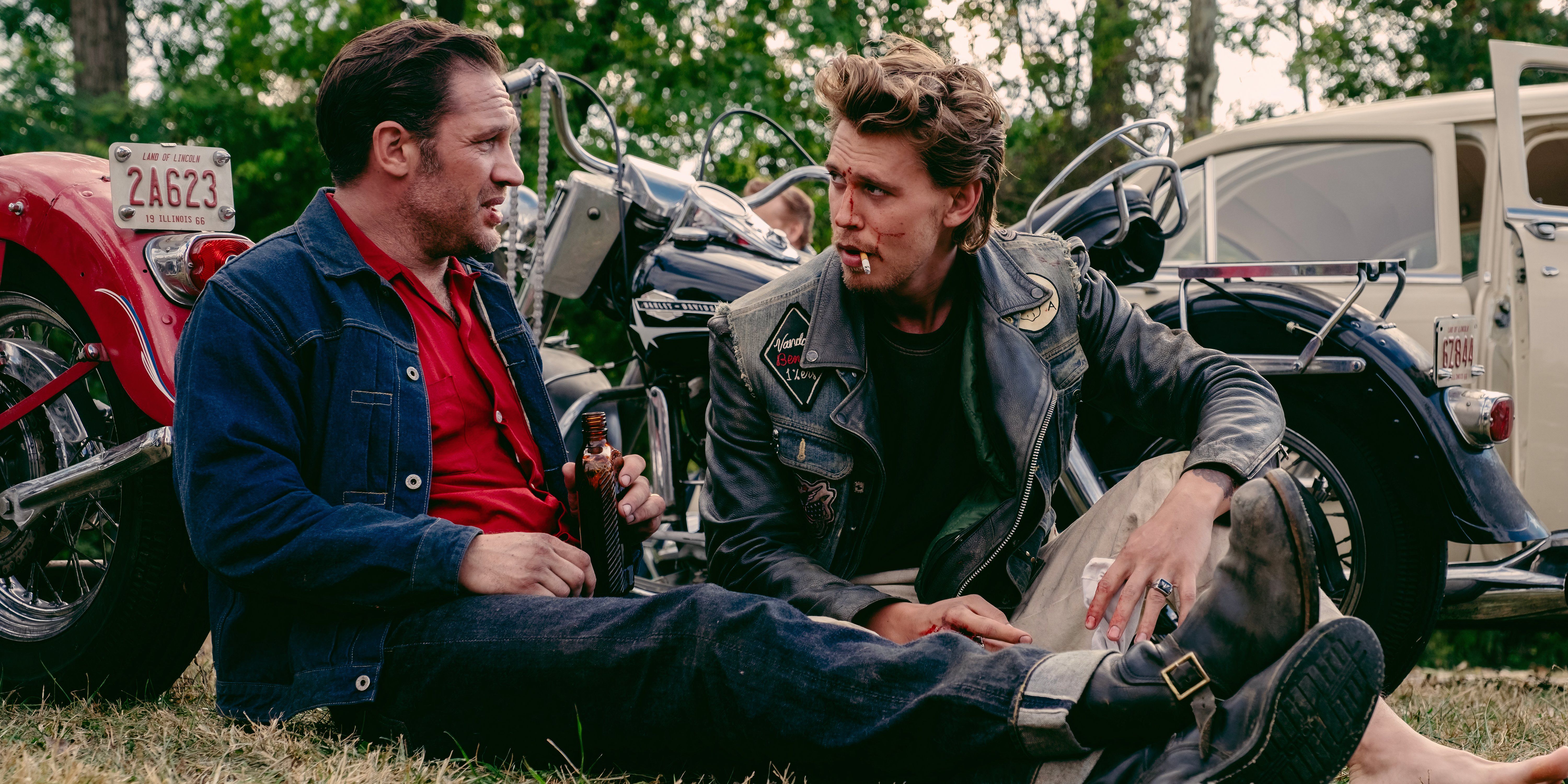 Johnny and Benny sit together talking on the grass in The Bikeriders movie still