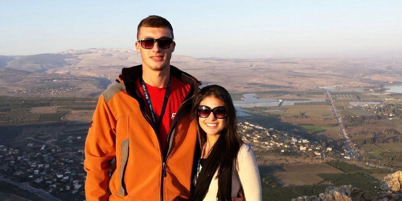 Loren in white top and Alexei Brovarnik in orange jacket smiling In 90 Day Fiance with scenic location in the back