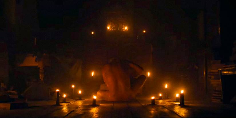 A naked man sitting on the floor in the dark, surrounded by candles in Nosferatu