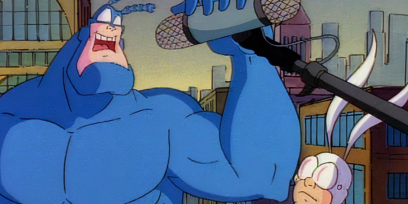 The Tick is speaking into a microphone while Arthur stands beside him. 