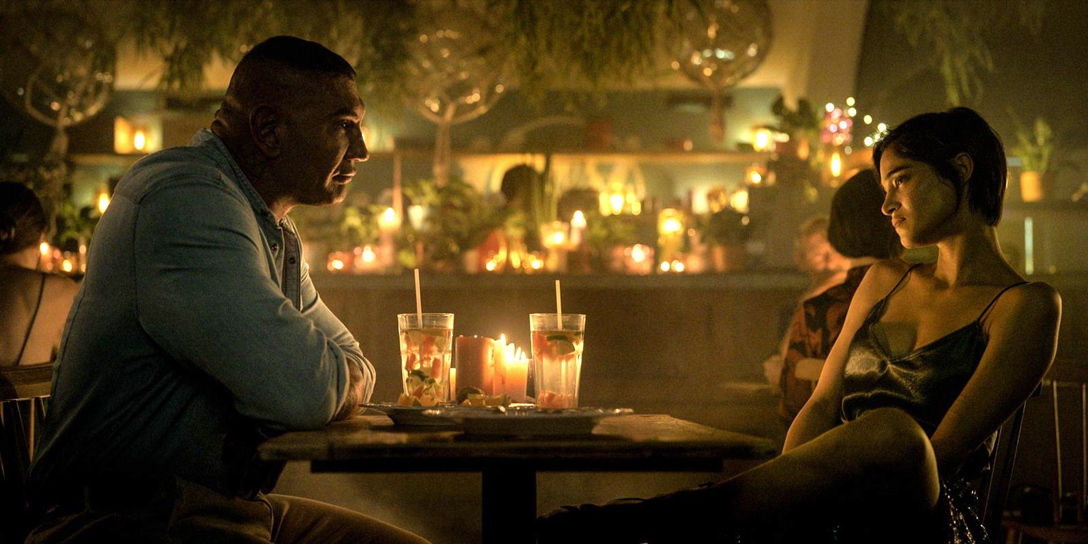 Dave Bautista e Sofia Boutella sentados à mesa em The Killer's Game