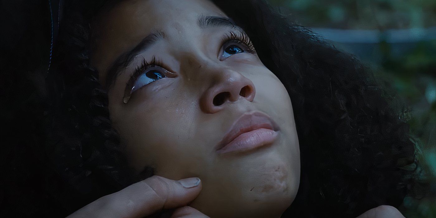 Rue, played by Amandla Stenberg, laying in Katniss' arms with a tear in her eye.