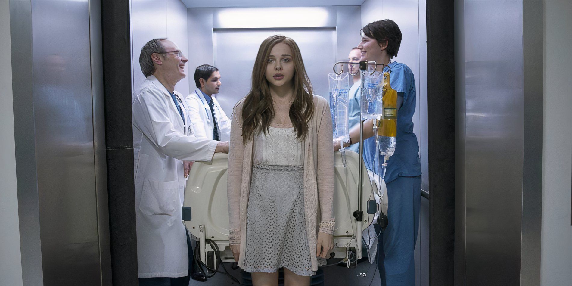 A young woman stands in front of doctors and nurses with a patient in an elevator in If I Stay