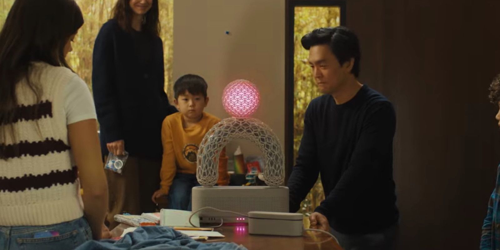 John Cho e sua família olham para Aia, um sistema operacional de IA que tem um arco de vidro e uma esfera rosa no topo, no filme Afraid