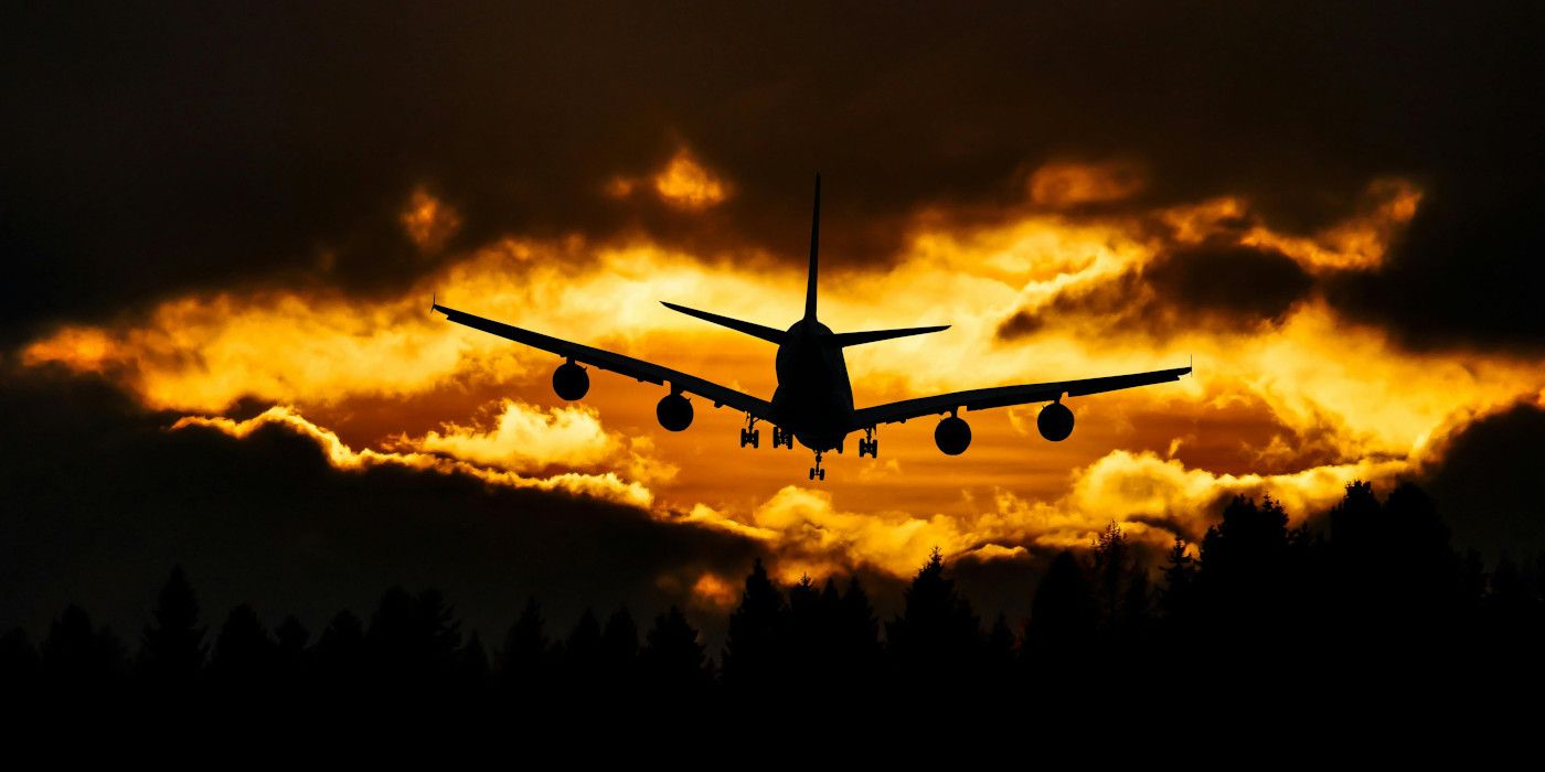 Uma imagem de um avião voando em direção a um céu laranja e nuvens escuras