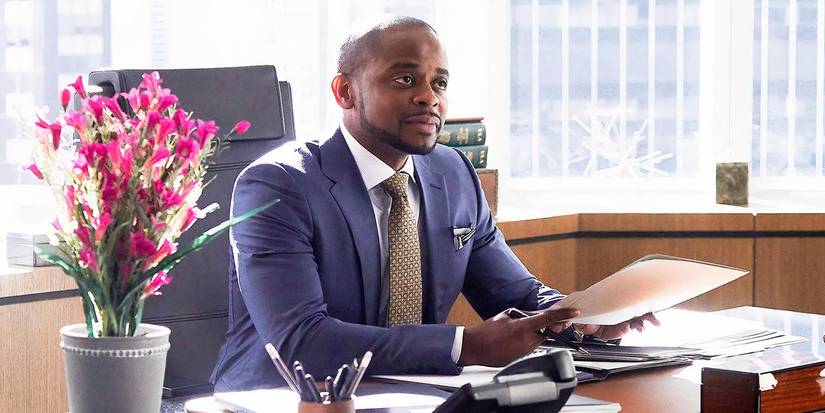 Alex Williams smiling at his desk in Suits