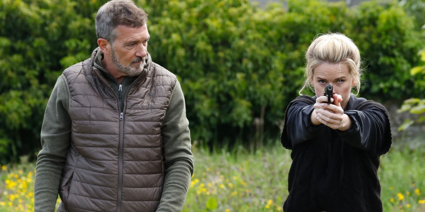 Antonio Banderas olha para Alice Eve, que aponta uma arma para frente, enquanto está do lado de fora em uma campina em Cult Killer-1