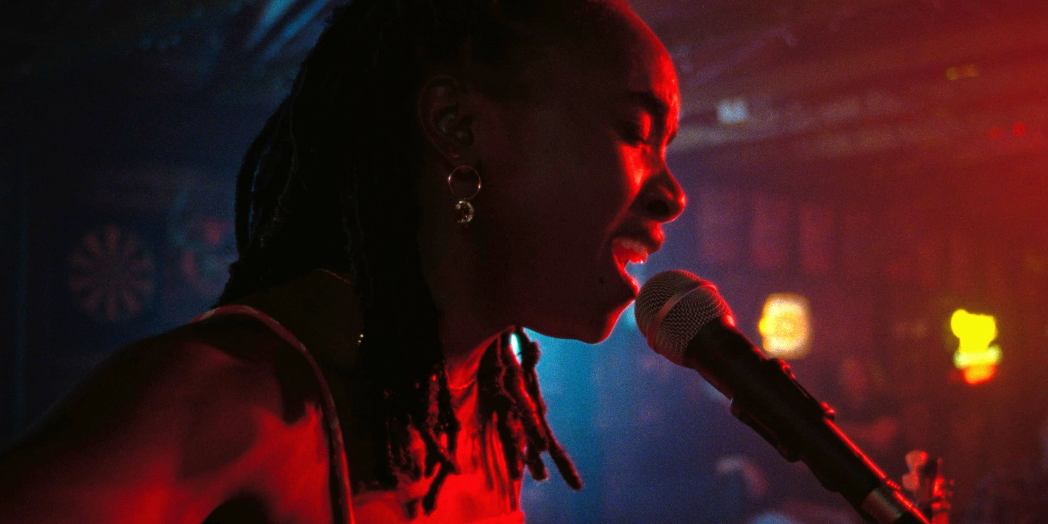 Dandelion sings into a microphone on stage with red lighting in Dandelion