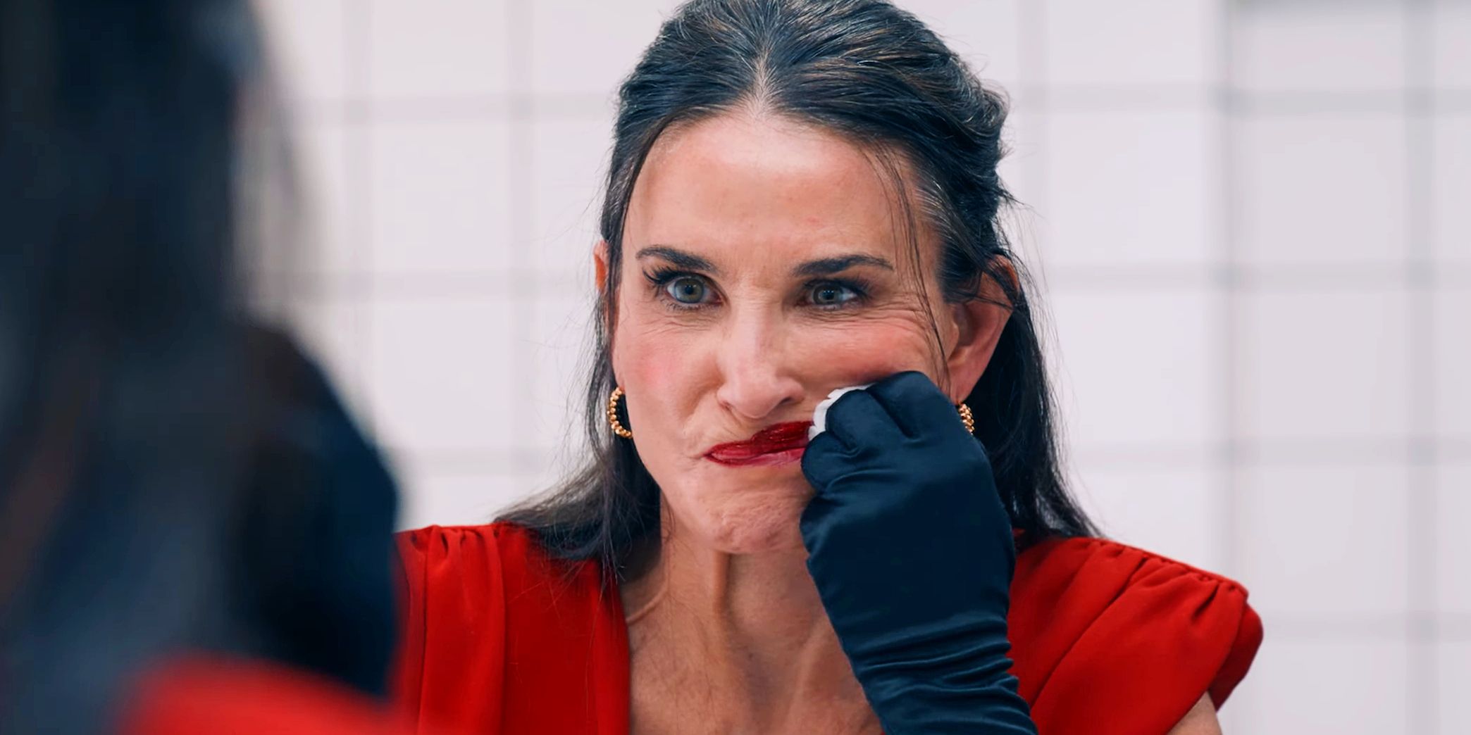 Demi Moore angrily smears her lipstick in the mirror in The Substance 