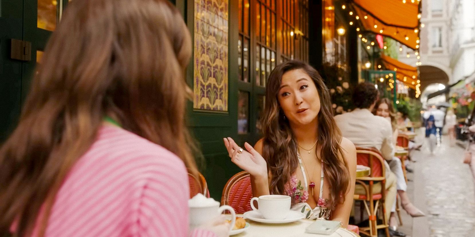 Mindy (Ashley Park) y Emily cotillean en un café en la temporada 4 de Emily's Paris