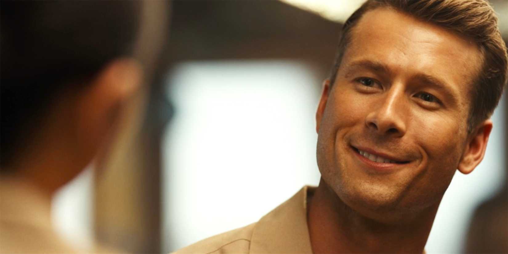 Hangman (Glen Powell) smiles while tilting his head to the side in Top Gun: Maverick