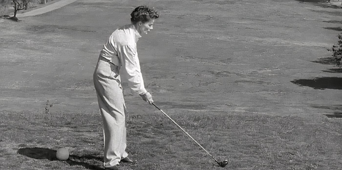 Katharine Hepburn se prepara para bater uma bola de golfe com seu taco. 