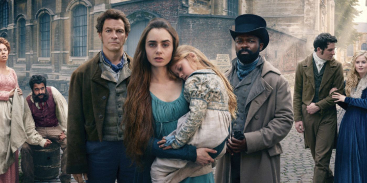 Lily Collins as Fantine in Les Mis TV show holding child Cosette and standing in a crowd of the ensemble for the show